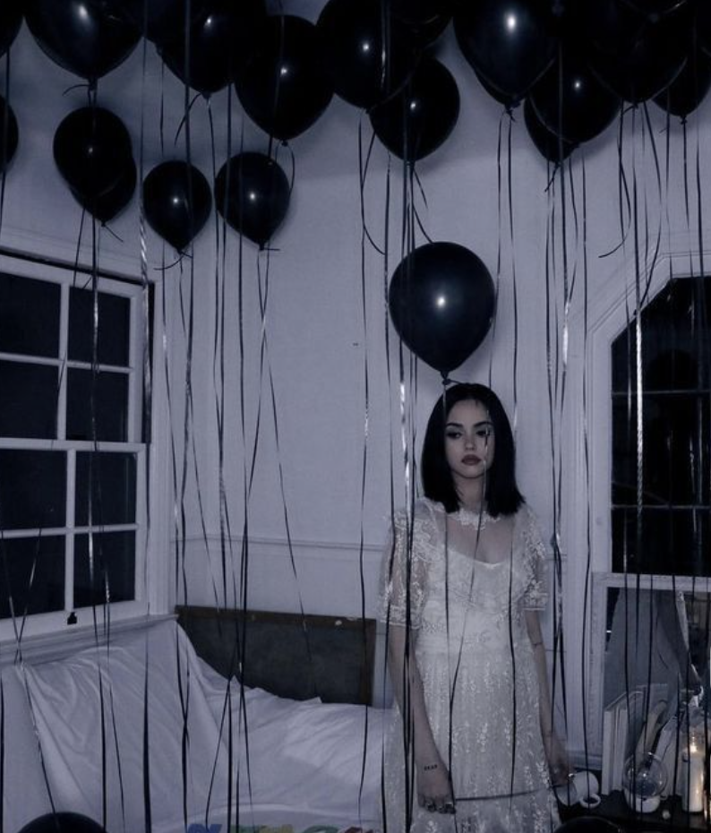 A girl in a white dress standing under black balloons