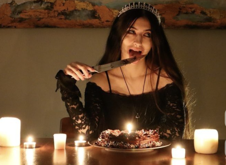 A girl in a crown biting a knife at a candlelit table