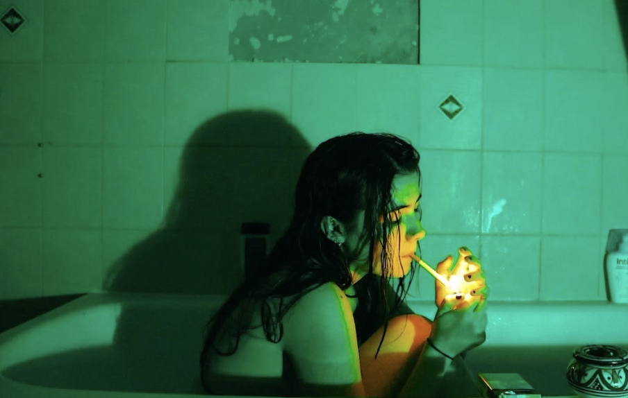 A girl in a bathtub in sick green light, holding a match