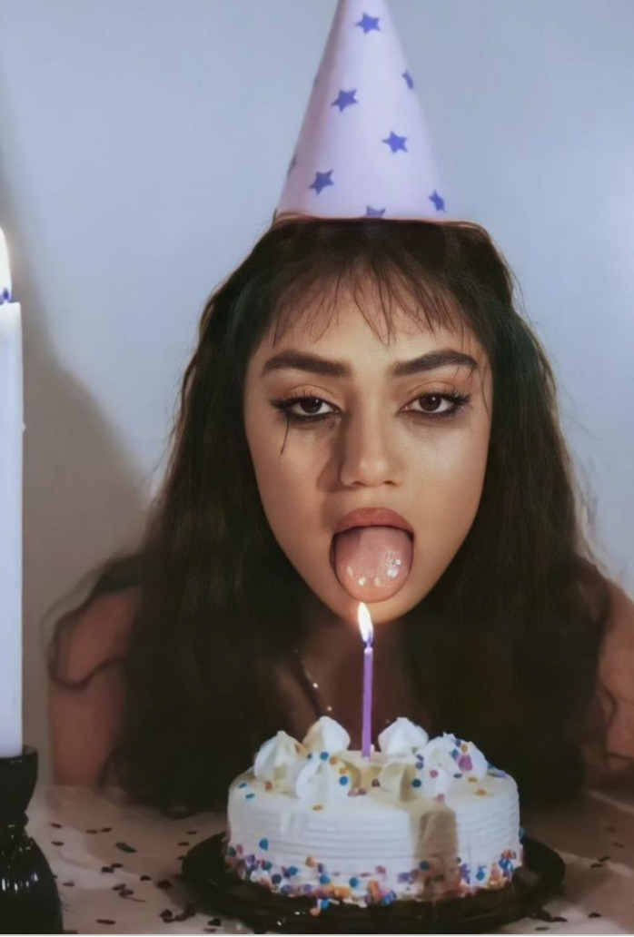 A girl in a party hat, tongue out, single candle